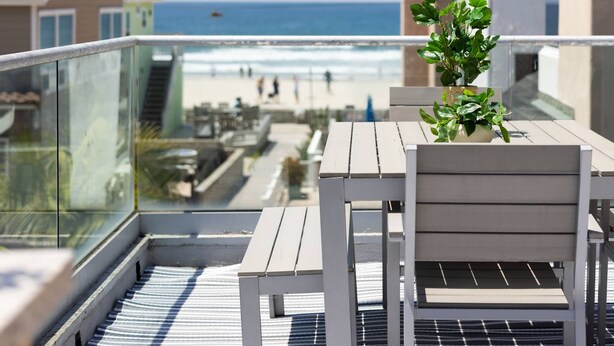 Un balcón con una mesa, sillas, una planta en maceta y vista a la playa y al océano.