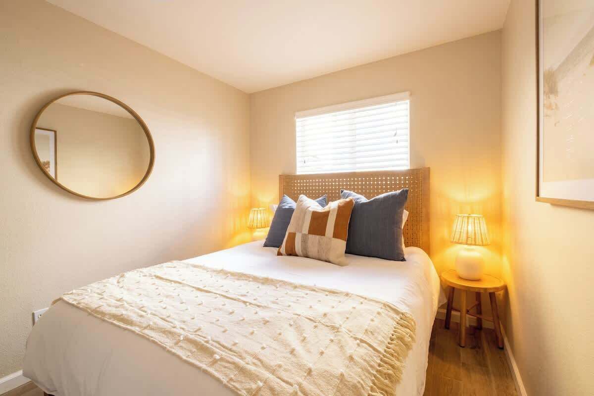 Ein Schlafzimmer mit einem Bett, einem runden Spiegel, einem Fenster mit Jalousien und zwei Nachttischlampen.
