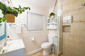 A bathroom with a white sink, toilet, and shower. There are two potted plants, one on the left and one on the right. - Sunny 3BR Seaside Escape | Beach & Bay Steps Away! (San Diego)