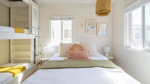 Quarto de hotel com beliche, uma cama de solteiro, mesa de cabeceira com abajur, janela com vista e luminária pendente.
