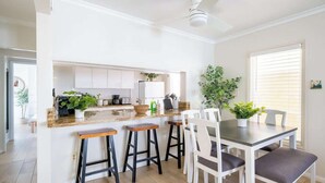 Uma cozinha moderna com armários brancos, bancada de granito e área de jantar com cadeiras e um banco brancos.