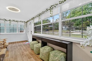 A bright room with large windows, a wooden floor, and green patterned cushions. - Walk to Downtown Mount Dora! Patio Oasis + King Bed! (Mount Dora)