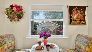 A cozy room with patterned sofas, a small round table with a vase of flowers, and a window with a view of a house. - Walk to Downtown Mount Dora! Patio Oasis + King Bed! (Mount Dora)