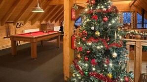 Un ambiente acogedor en el interior, con techo de madera, una mesa de billar y un árbol de Navidad decorado.