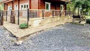Una cabaña de madera con techo inclinado, un balcón y un camino de grava.
