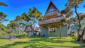 A two-story wooden house with a balcony, surrounded by a well-maintained lawn and trees.