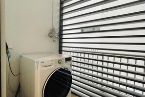 A laundry machine in a room with a window with horizontal blinds. - Nanahousing-Nice Apartment near Korea Town & Chinese Area (Hanoi)