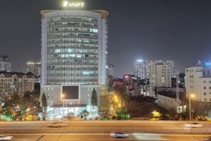 A high-rise building with a prominent sign at the top, surrounded by other buildings and a highway. - Nanahousing-Nice Apartment near Korea Town & Chinese Area (Hanoi)