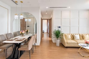 A modern living room with a sofa, a dining table with chairs, and a potted plant. - Nanahousing-Nice Apartment near Korea Town & Chinese Area (Hanoi)