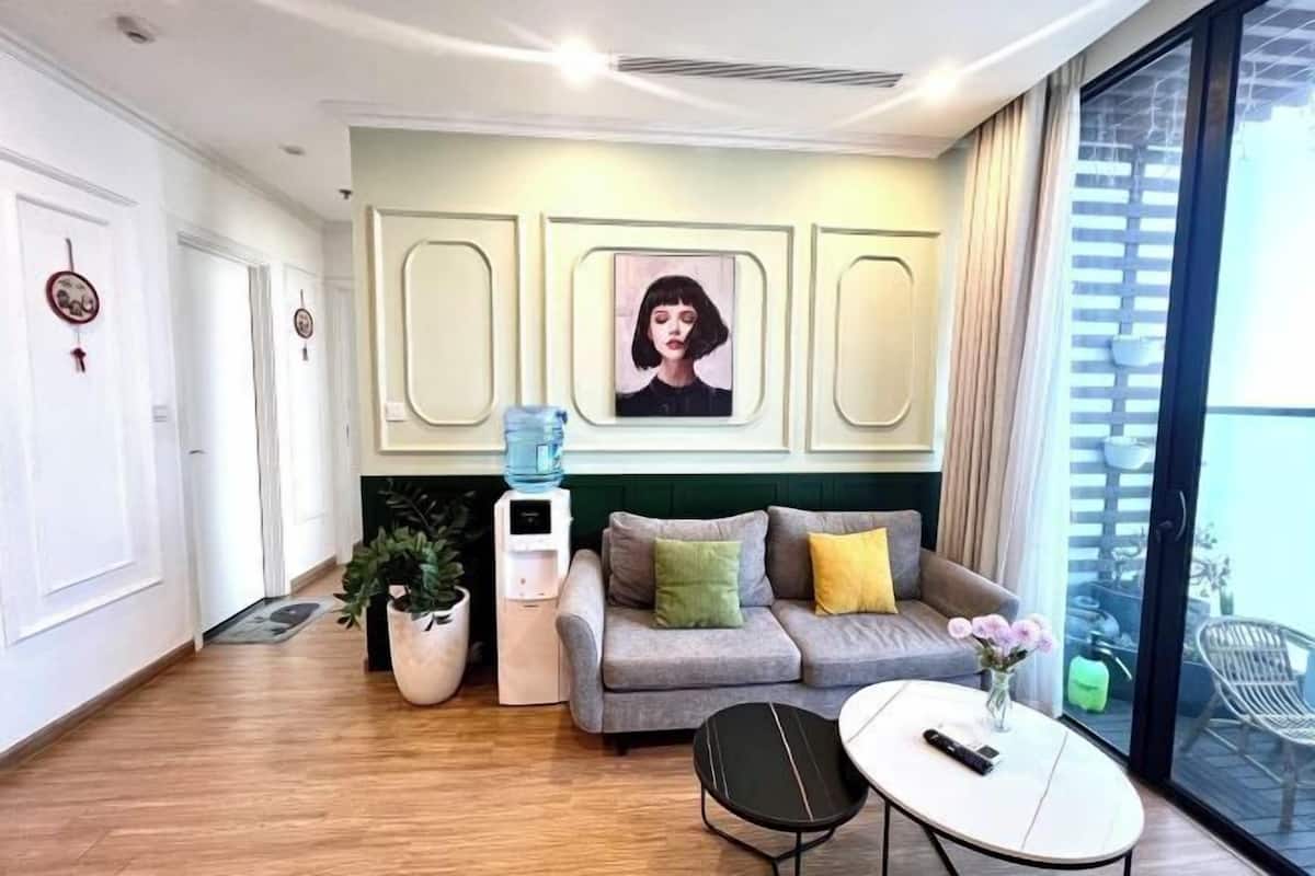 Uma sala de estar moderna com um sofá cinzento, uma mesa pequena, um dispensador de água e uma planta em vaso.