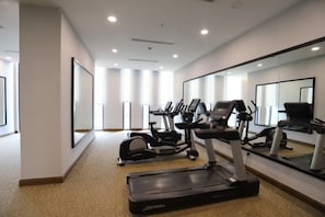 Une salle de sport moderne, équipée d’appareils de cardio, dotée d’un mur miroir et d’un sol recouvert de moquette.
