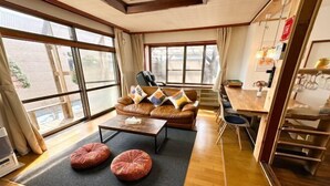 A modern living room with a brown leather sofa, two round ottomans, a wooden coffee table, and a dining area with a wooden table and chairs. - HAGINOTCHI (Shiraoi District)