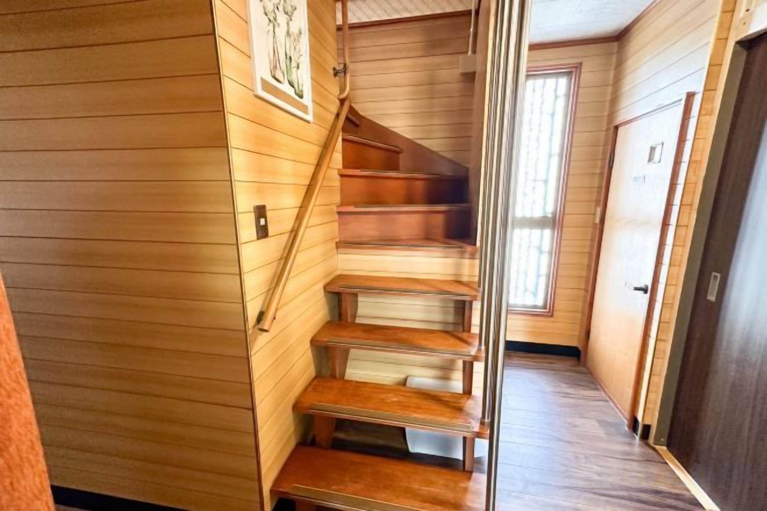 A wooden staircase with a handrail, leading to a door with a sign.