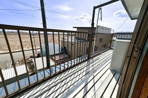 A balcony with a metal railing, a view of a building with a blue roof, and a clear sky. - HAGINOTCHI (Shiraoi District)