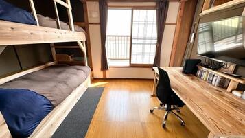 A room with bunk beds, a desk with a computer, and a window.