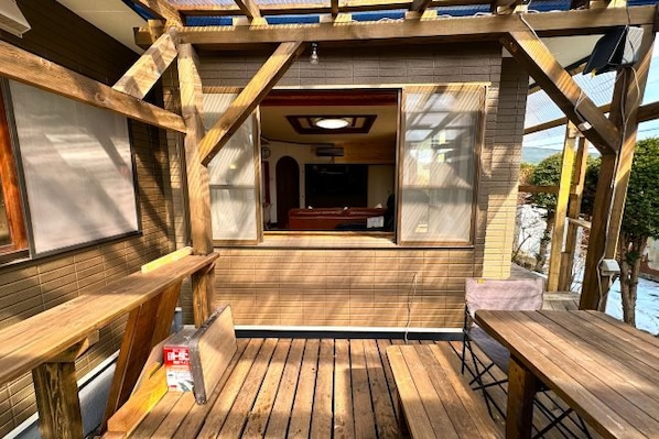 Terraza de madera con vista a una piscina y un área de descanso cubierta.