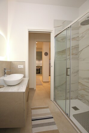 Un baño moderno con un lavamanos grande de color blanco, una cabina de ducha con paredes de vidrio y una paleta de colores neutros.