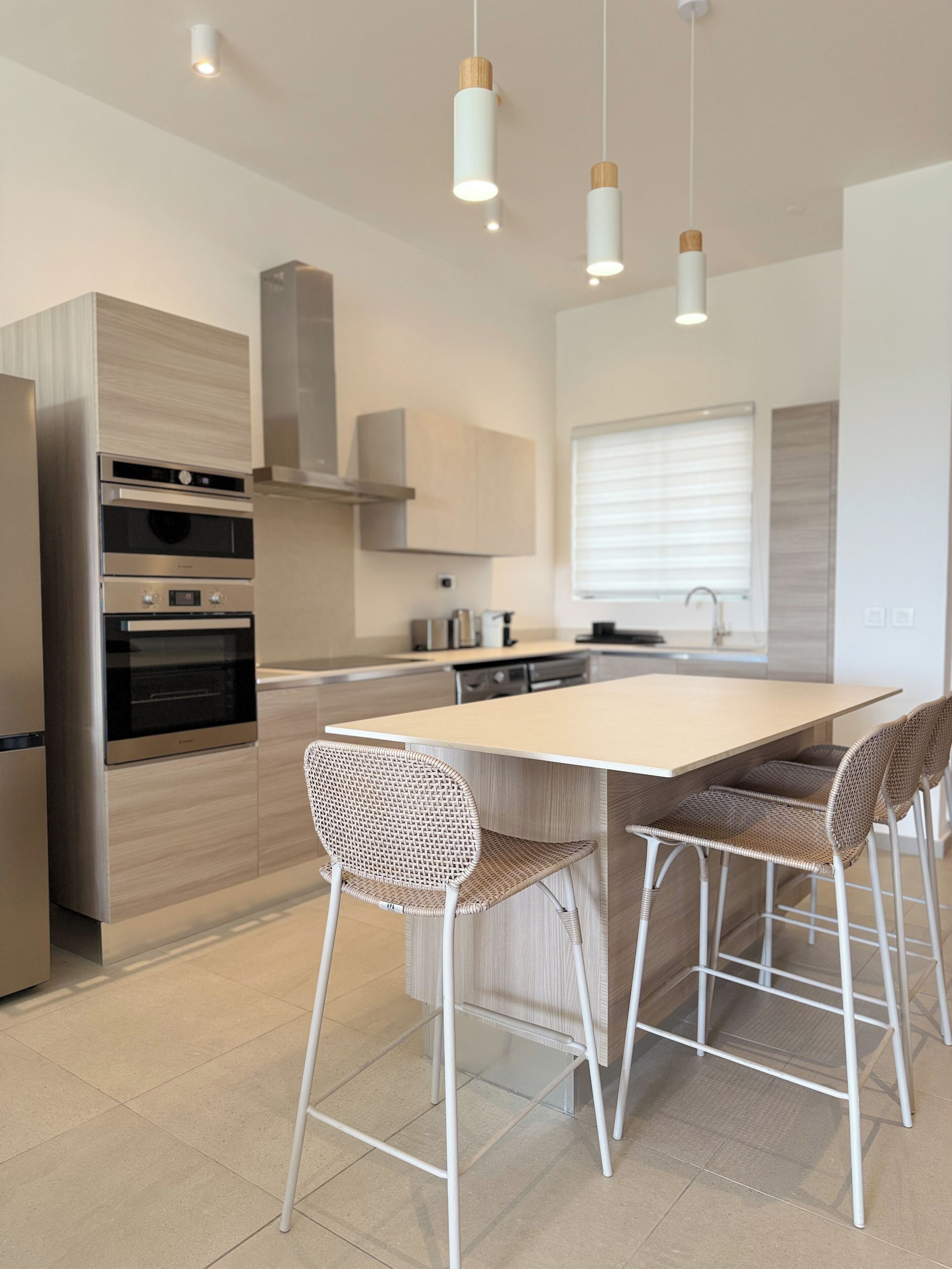Una cocina moderna con electrodomésticos de acero inoxidable, una isla grande con taburetes de bar e iluminación colgante.