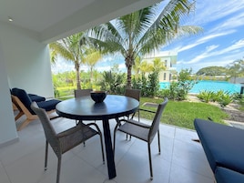 Un patio con una mesa redonda y sillas de mimbre, con vistas a una piscina y abundante vegetación.
