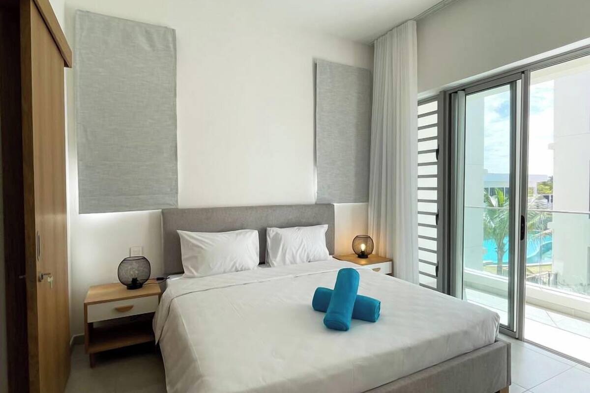 Un hotel moderno con una cama grande, una mesita de noche, una lámpara y vistas a una piscina a través de una puerta corrediza de vidrio.