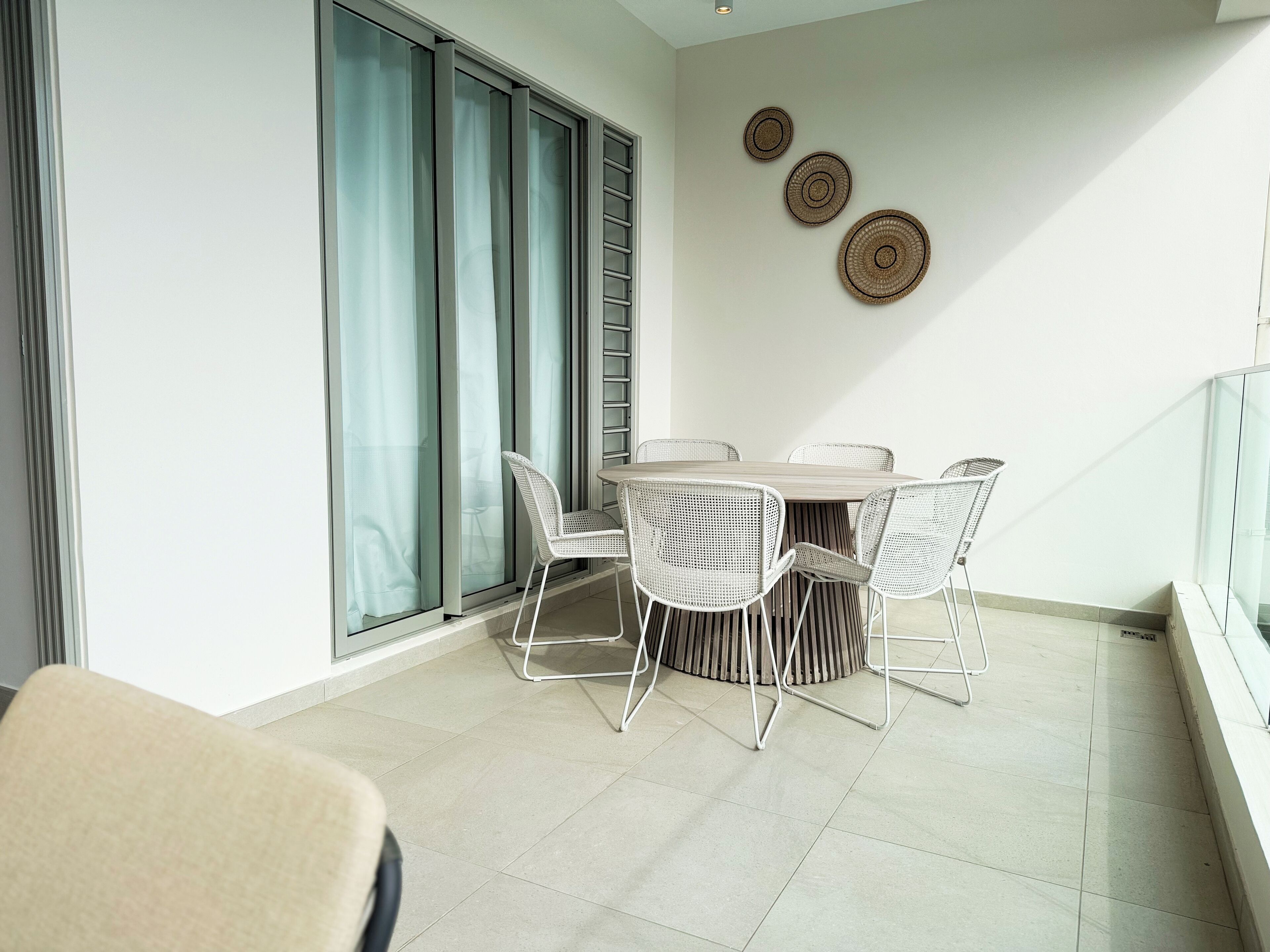 A balcony with a dining table and chairs, a sliding glass door, and three woven wall decorations.