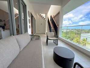Una sala de estar moderna con un sofá, una silla y una mesa redonda, una escalera y un balcón con vistas.