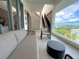 Una sala de estar moderna con un sofá, una silla y una mesa redonda, una escalera y un balcón con vistas.