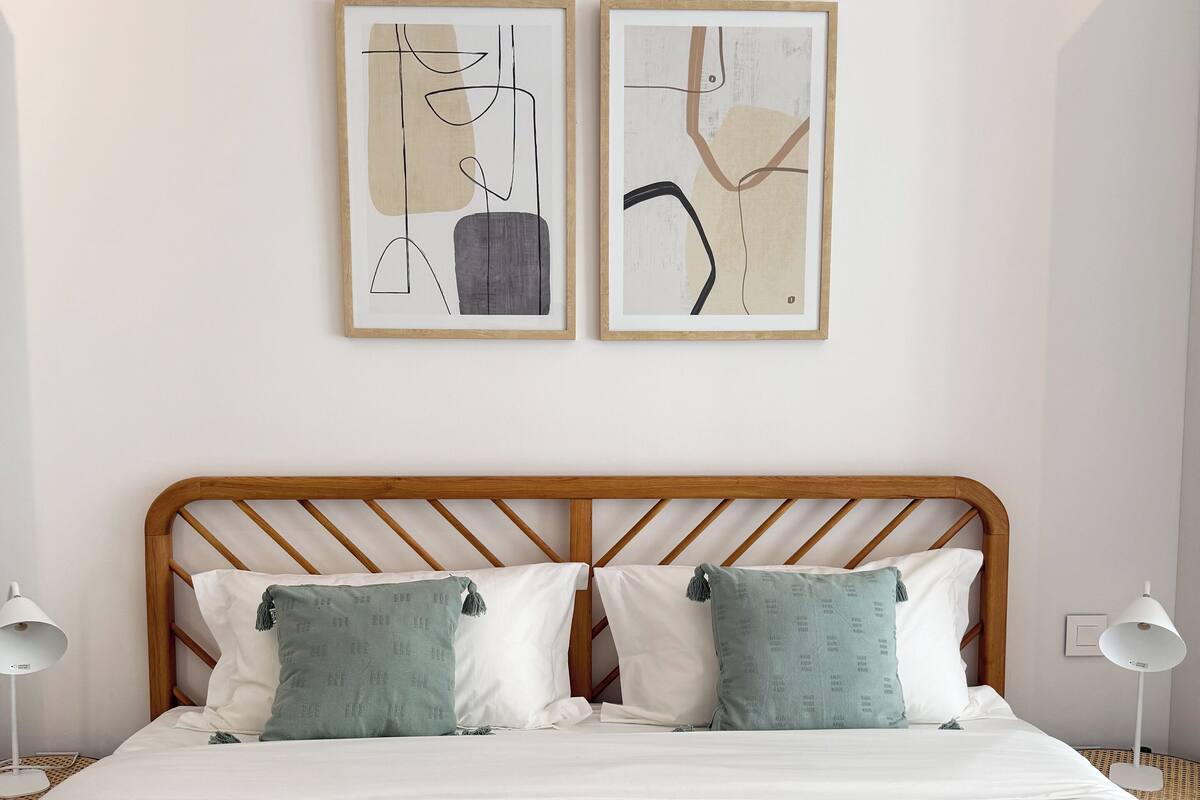 Una cama bien hecha con una colcha azul a rayas, dos almohadas y dos obras de arte abstracto en la pared de arriba.