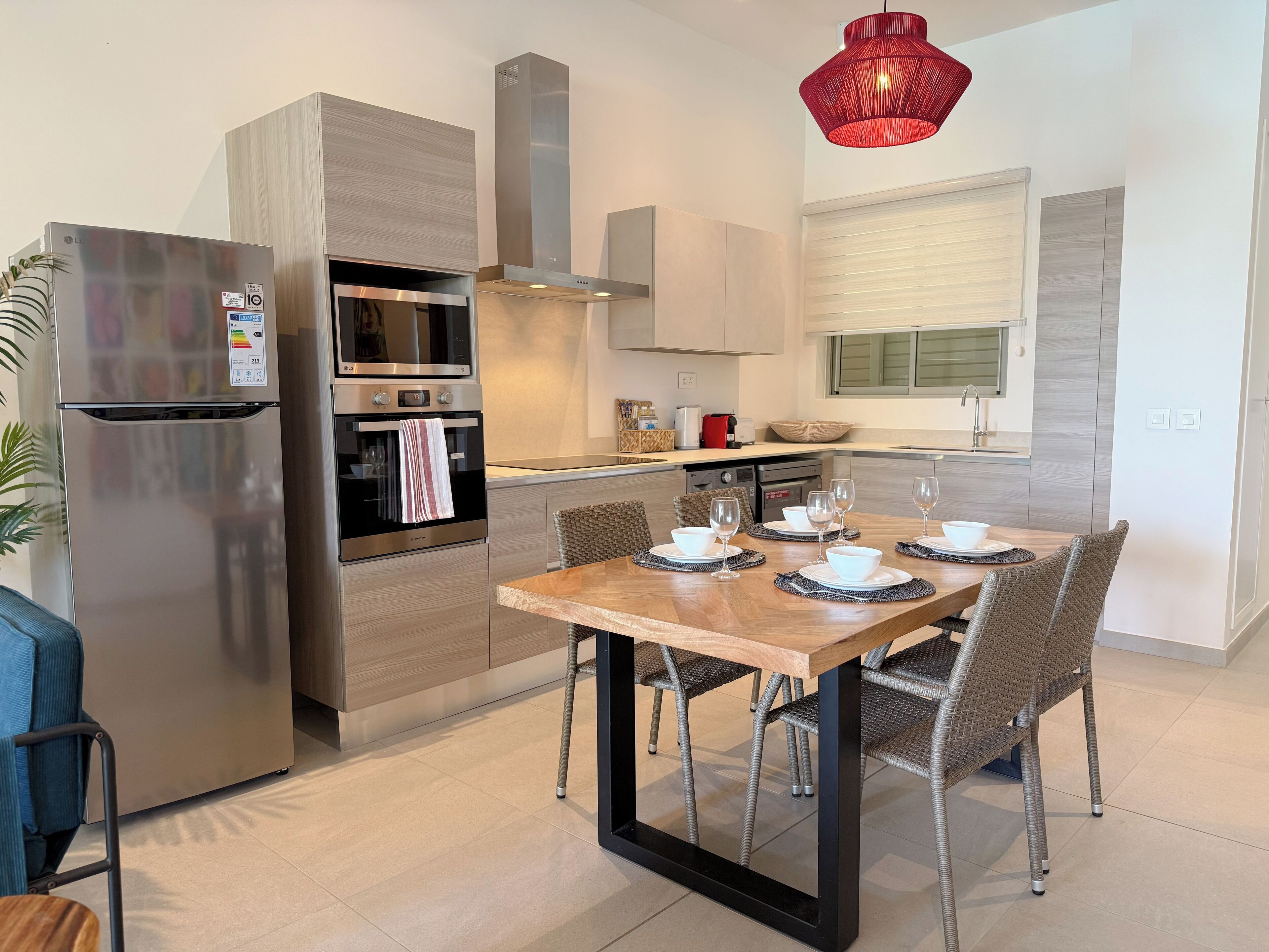 Una cocina moderna con electrodomésticos de acero inoxidable, una mesa de comedor para cuatro personas y una lámpara colgante roja.