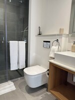 Un baño moderno con cabina de ducha de vidrio, inodoro blanco y tocador de madera con lavabo.