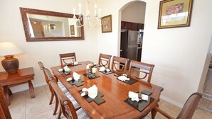 A dining room with a wooden table set for six, surrounded by chairs. A chandelier hangs above, and a large mirror is on the wall. - Lakeside Villa 5 Bedroom Home (Davenport)