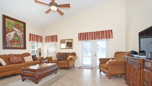 A living room with a ceiling fan, a large painting, a sofa set, a coffee table, and a cabinet. - Lakeside Villa 5 Bedroom Home (Davenport)