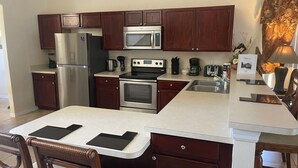 A modern kitchen with dark wood cabinets, stainless steel appliances, and a white countertop. - Lakeside Villa 5 Bedroom Home (Davenport)