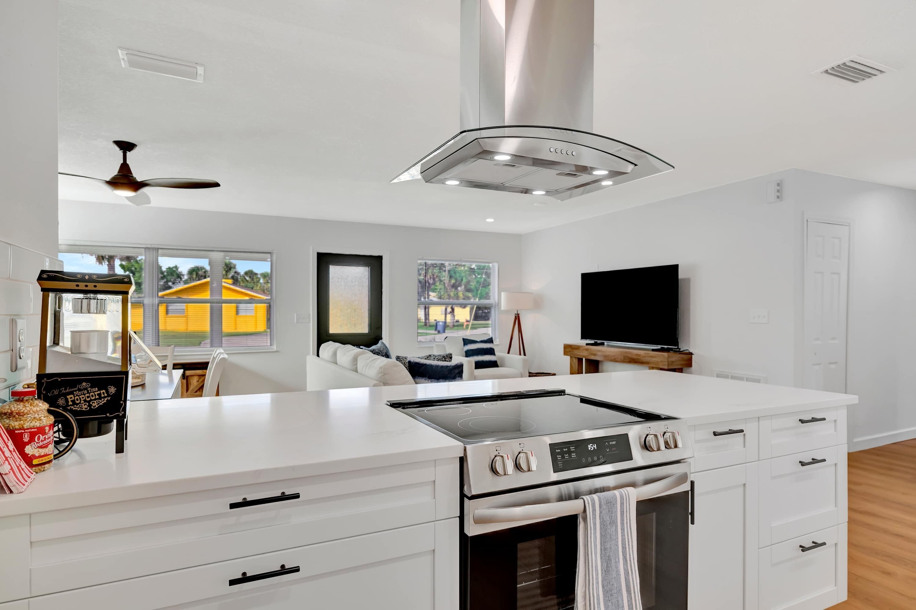 A modern kitchen with a central island, built-in oven, and a large window offering a view of a yellow building.