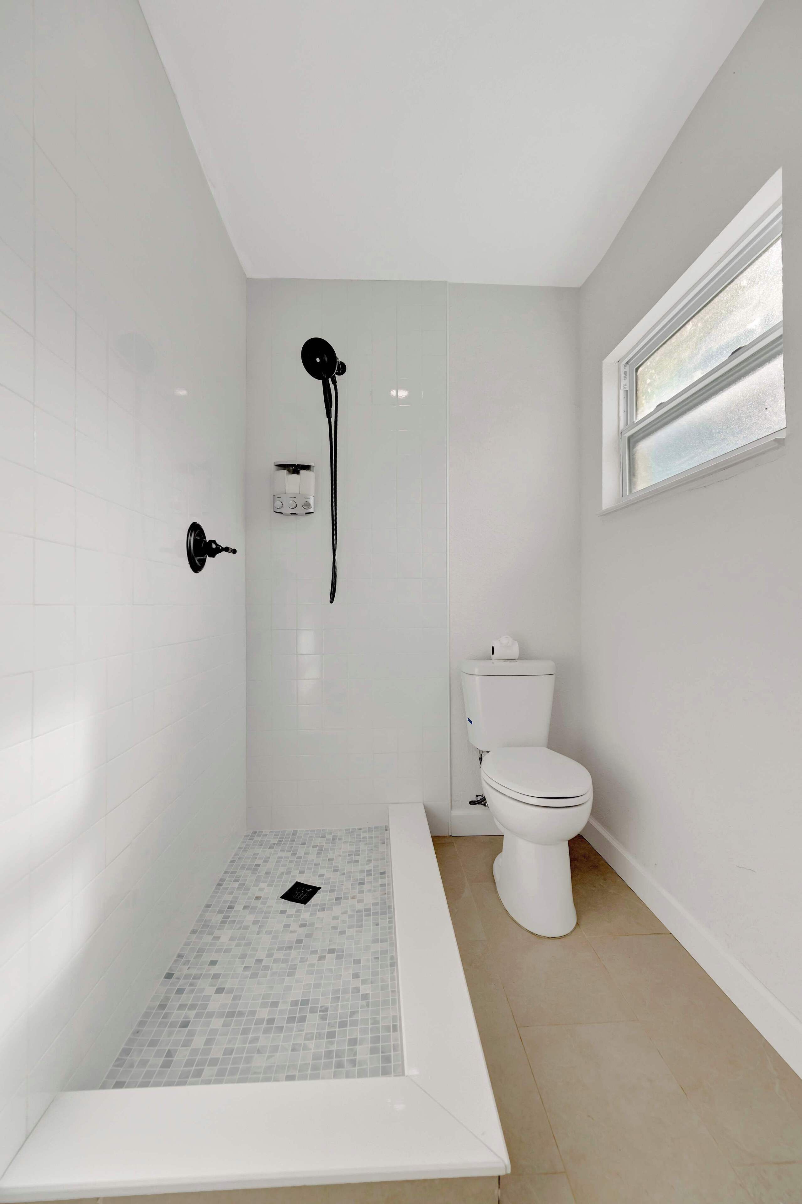 A modern bathroom with a walk-in shower, a toilet, and a window.
