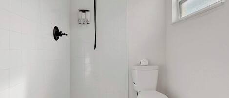 A modern bathroom with a walk-in shower, a toilet, and a window.