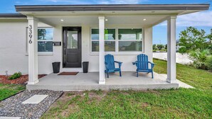 Une maison moderne dotée d’un porche abrité, de deux fauteuils Adirondack bleus et d’une pelouse bien entretenue.