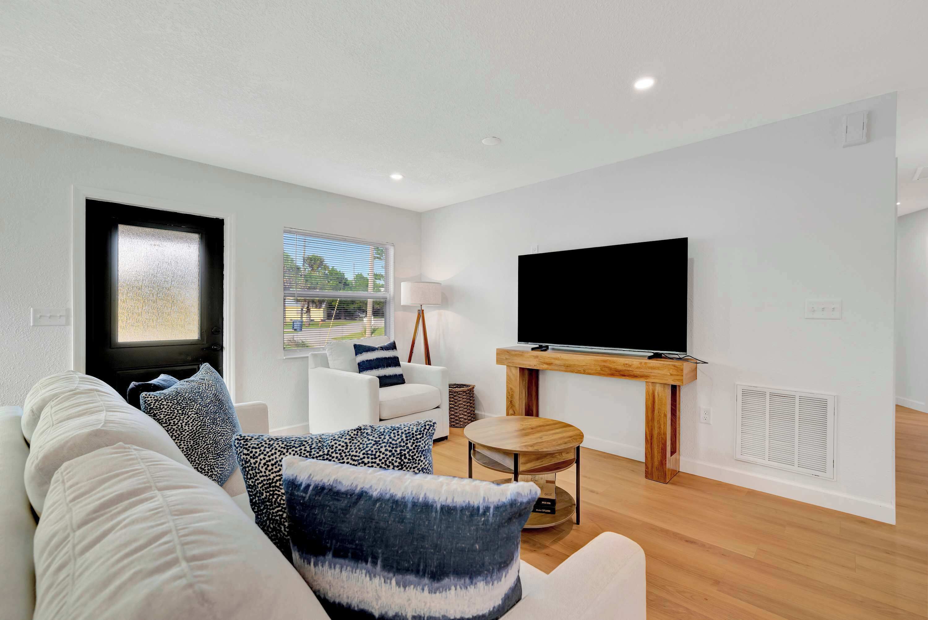 A modern living room with a white sofa, a coffee table, and a flat-screen TV mounted on the wall.