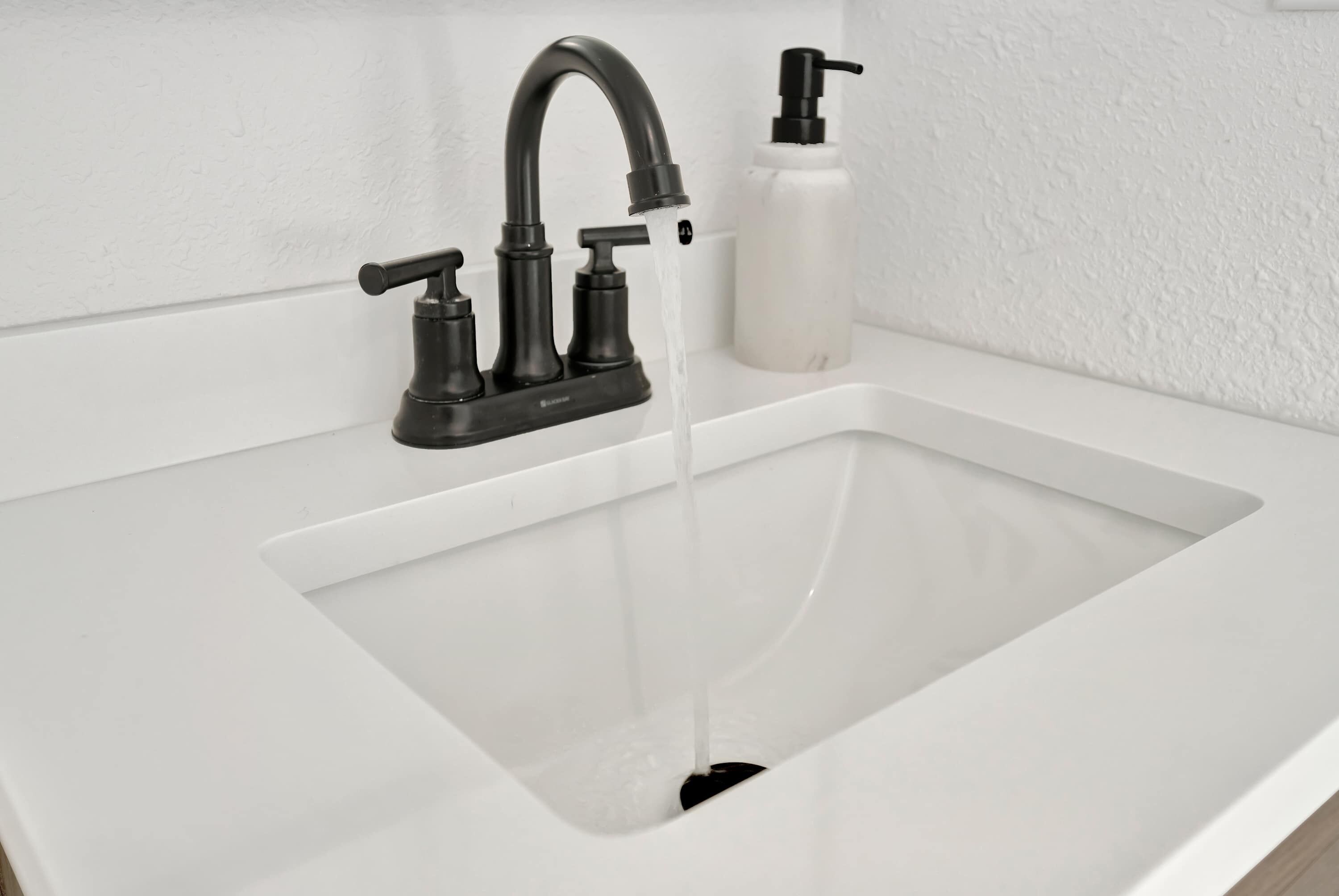 A modern bathroom sink with a black faucet, a soap dispenser, and a white countertop.