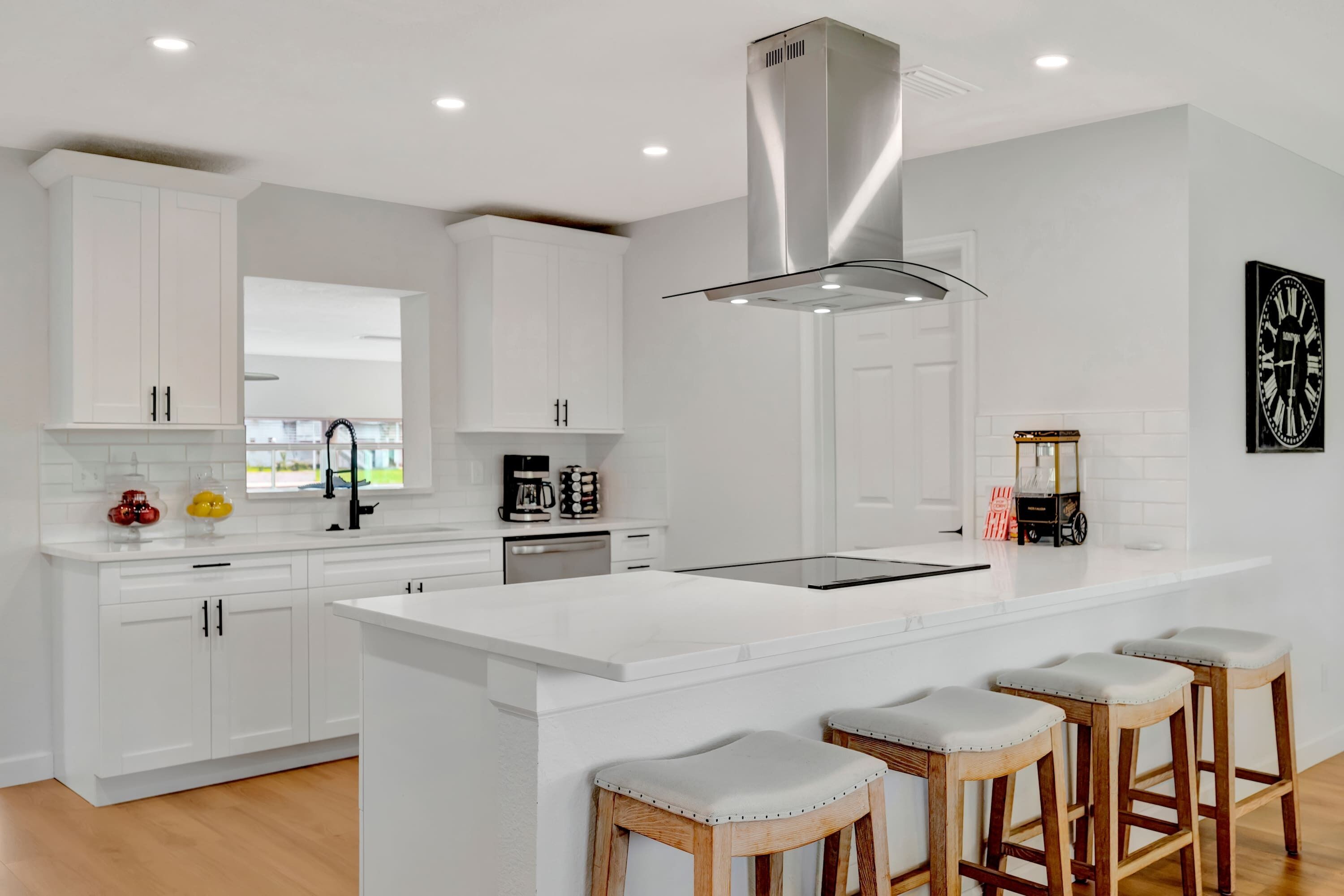 A modern kitchen with white cabinetry, a central island with bar stools, and a stainless steel range hood.