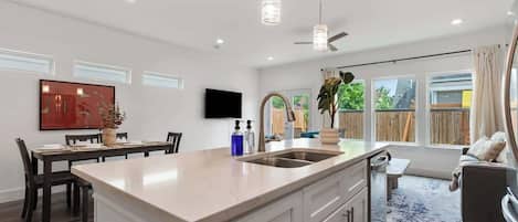 A modern kitchen with a central island, pendant lighting, and a dining area with a TV.