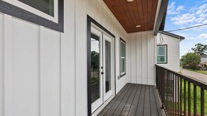 Eine überdachte Veranda mit Holzboden, weißer Fassade und einem schwarzen Geländer.