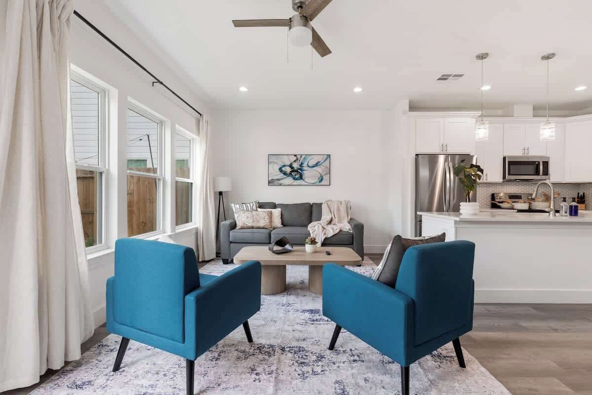 Uma sala de estar moderna com um sofá e duas poltronas, uma mesa de centro e um ventilador de teto.