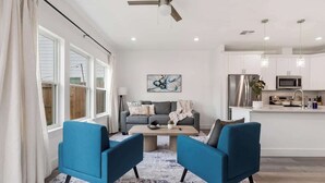 Ein modernes Wohnzimmer mit einer Couch, zwei Sesseln, einem Couchtisch und einem Deckenventilator.