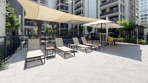 An outdoor patio area with lounge chairs and umbrellas, surrounded by high-rise residential buildings. - Dubai Creek Harbour Sleeps 4 With Private Balcony (Dubai)