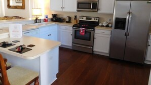 Una cocina con armarios blancos, un refrigerador de acero inoxidable, un microondas, un horno y una cafetera.