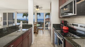 A kitchen with a large island, stainless steel appliances, and a view of the ocean. - Kona Coffee Villas E246 2 Bedroom Condo (Holualoa)