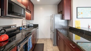 A compact kitchen with stainless steel appliances, wooden cabinets, and a granite countertop. - Kona Coffee Villas E246 2 Bedroom Condo (Holualoa)