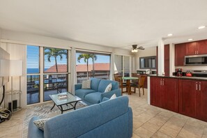A spacious living area with a blue sofa, a dining table, and a kitchen with wooden cabinets and a microwave. - Kona Coffee Villas E246 2 Bedroom Condo (Holualoa)