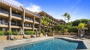 A hotel with a swimming pool, multiple balconies, and palm trees. - Kona Pacific D526 1 Bedroom Condo (Kailua-Kona)
